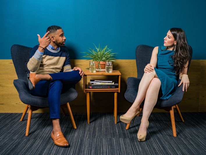 Woman Wearing Teal Dress Sitting on Chair Talking to Man